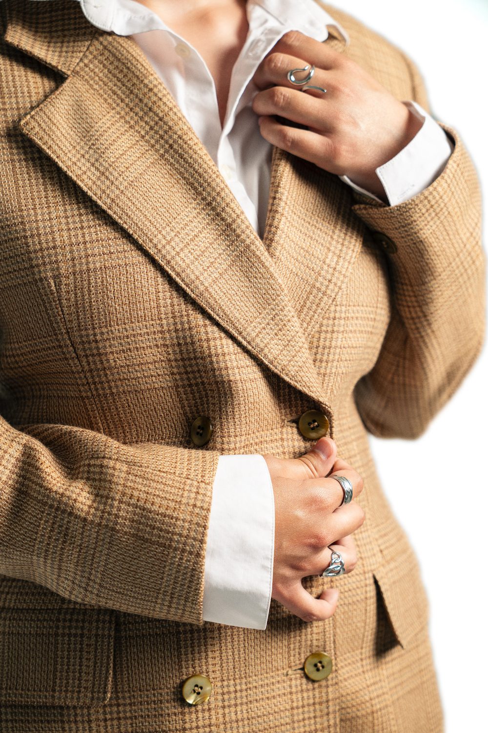 Close up of a camel checked blazer with gold buttons, white shirt and silver rings