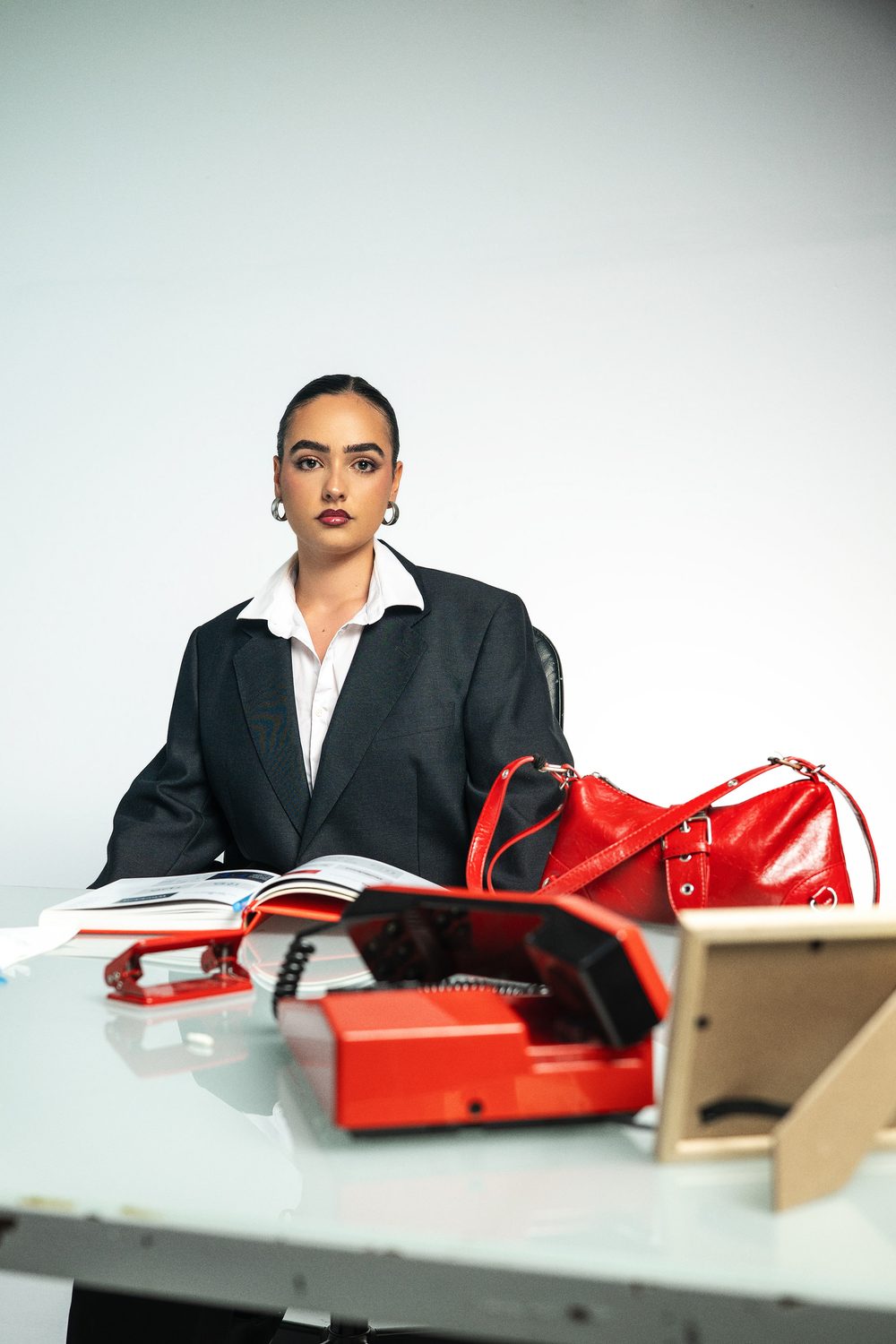 Aida seated at a glass desk with a red bag and vintage red telephone