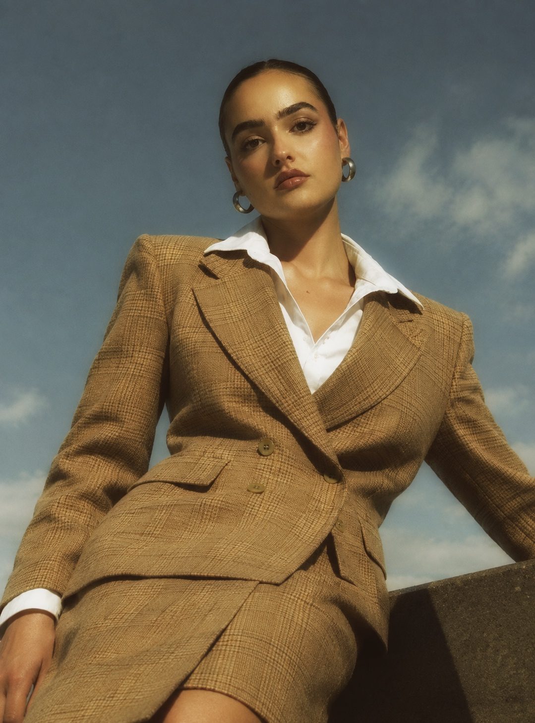Low angle portrait of Aida in a camel checked blazer against the sky