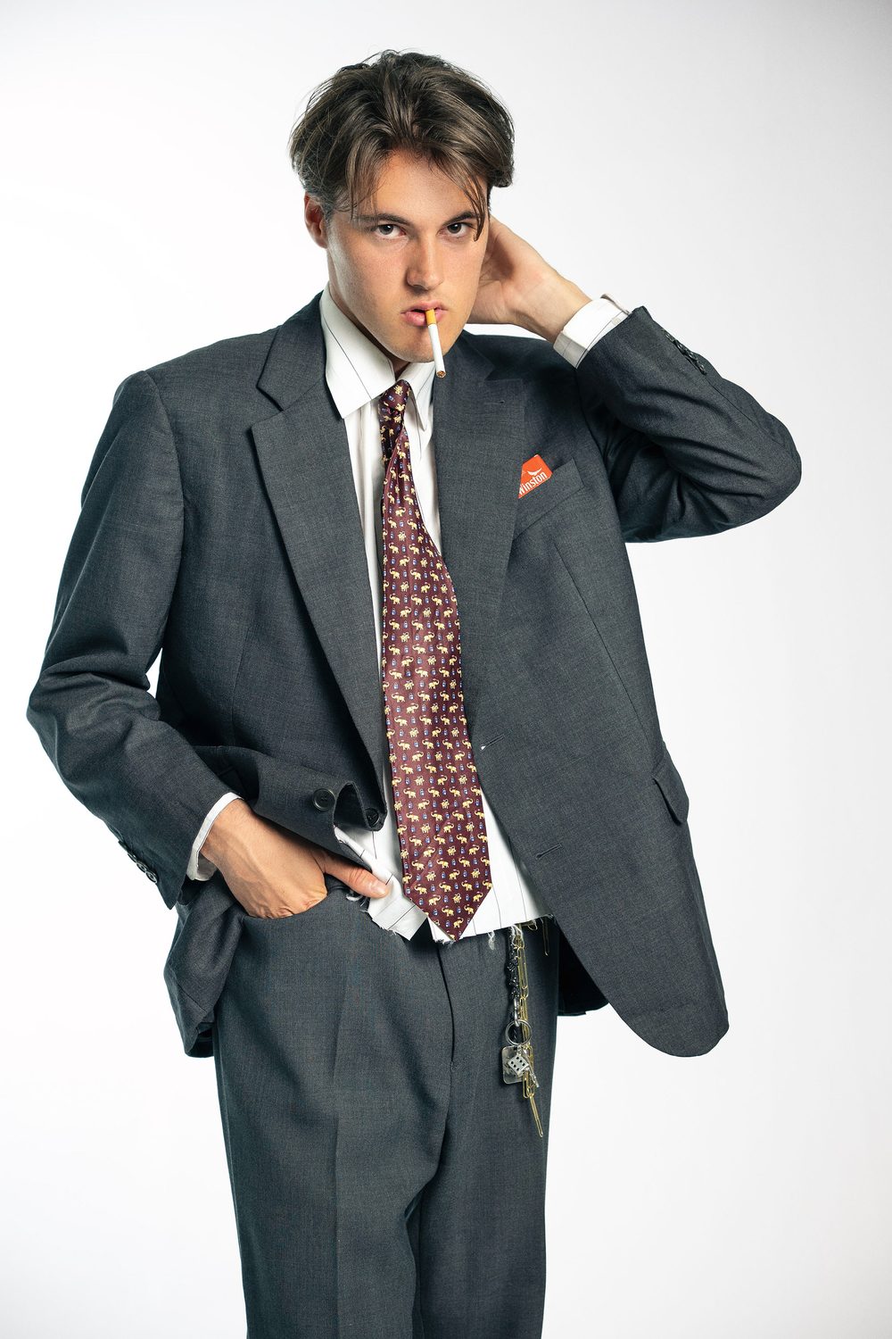 Marc in an oversized grey suit and burgundy patterned tie with a cigarette in his mouth