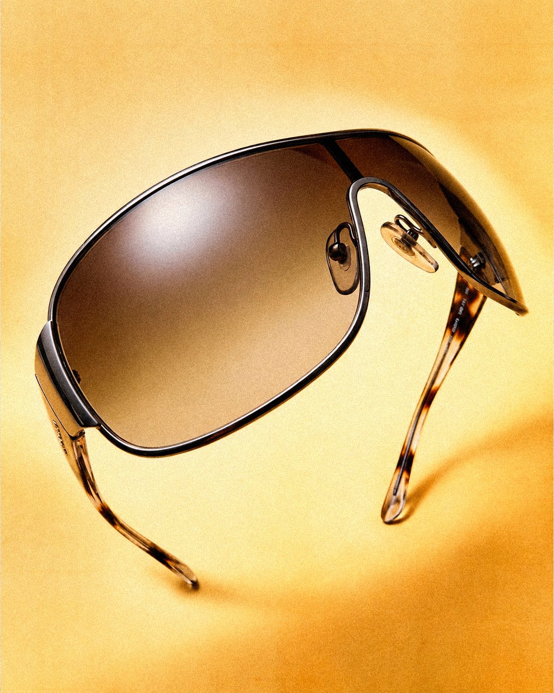 Vintage Prada shield sunglasses with tortoiseshell arms floating on a warm yellow background